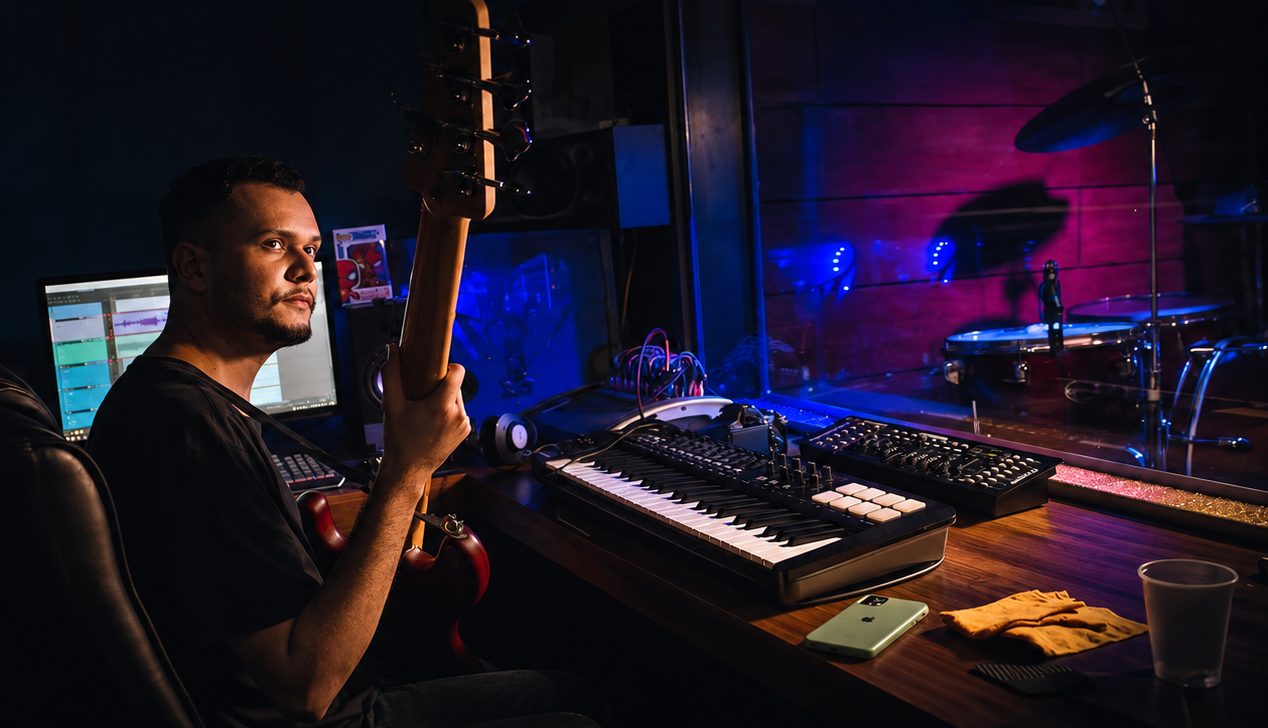 Baixista na sala técnica do Faria Studio, com teclado controlador e monitores