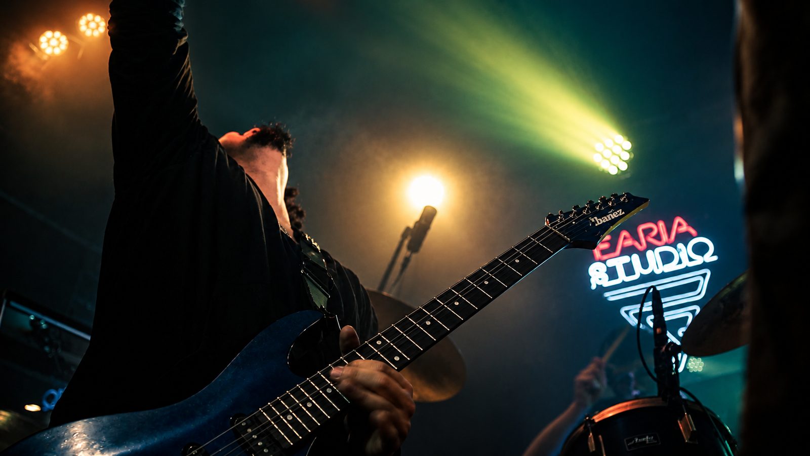Guitarra em primeiro plano com luzes de palco e a placa neon