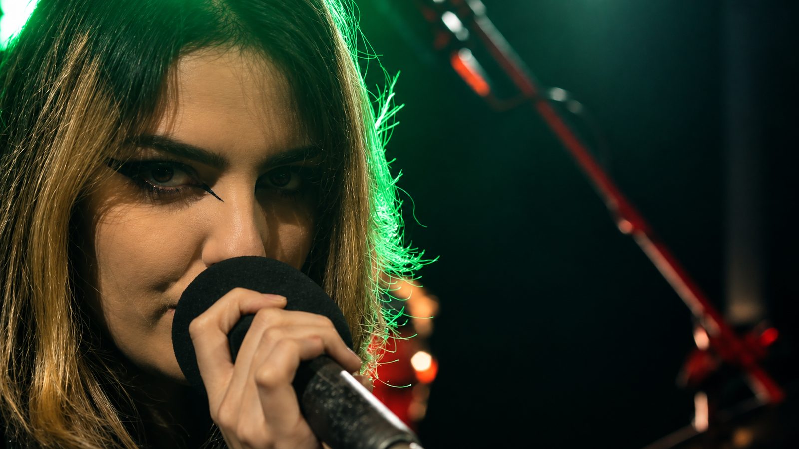 Vocalista cantando de perto ao microfone sob luz verde